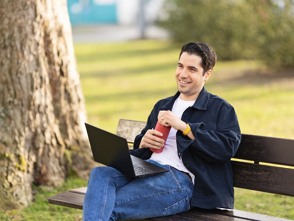 Seorang karyawan Henkel duduk di bangku di taman dan bekerja di laptopnya. 