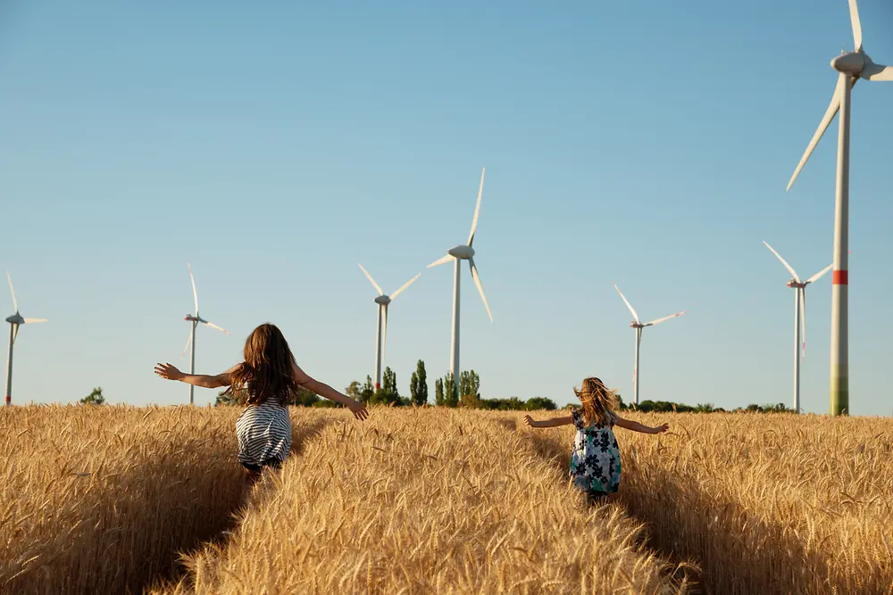 Gadis-gadis berlari melalui lapangan menuju turbin angin.