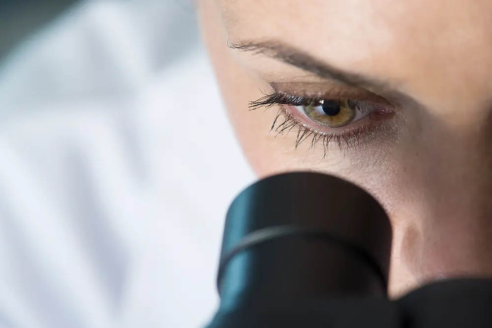 Mata seorang wanita yang sedang melihat ke dalam mikroskop