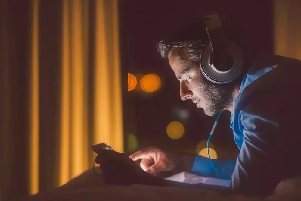Seseorang memakai headphone dan bekerja dengan peralatan elektronik di lingkungan gelap.