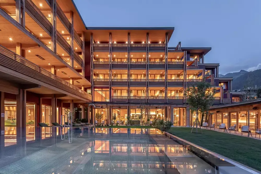 Gedung komersial modern dengan eksterior yang diterangi dan kolam refleksi saat senja.